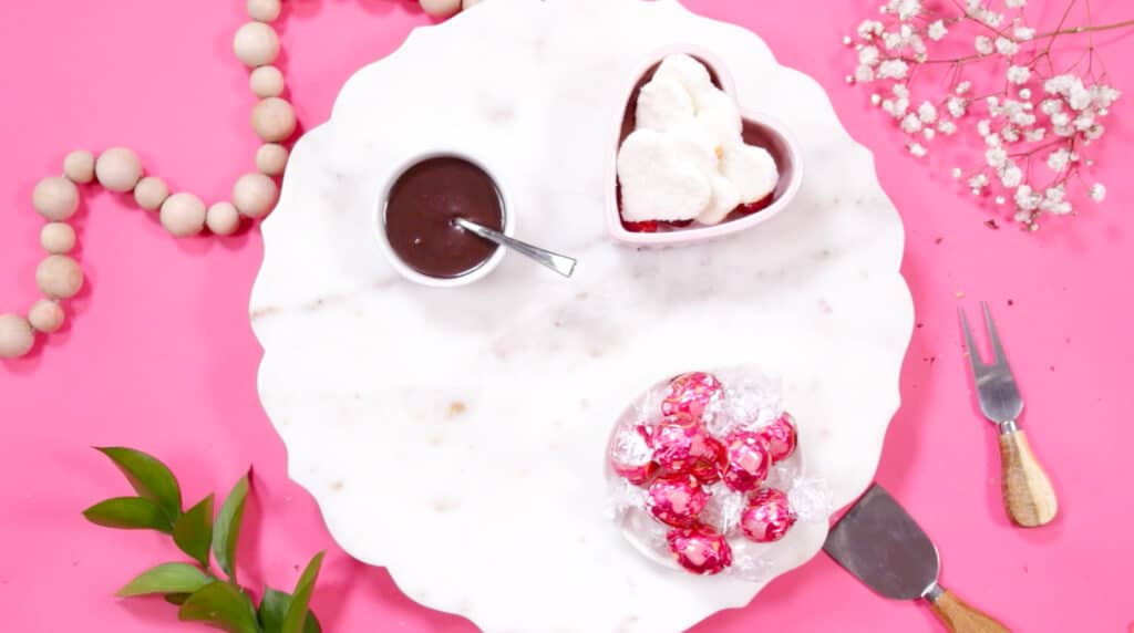 Dessert Charcuterie Board by popular Utah craft blog, Sweet Red Poppy: image of a white marble board set with wrapped chocolate candies, heart shaped marshmallows, and a white ceramic bowl filled with melted chocolate. 