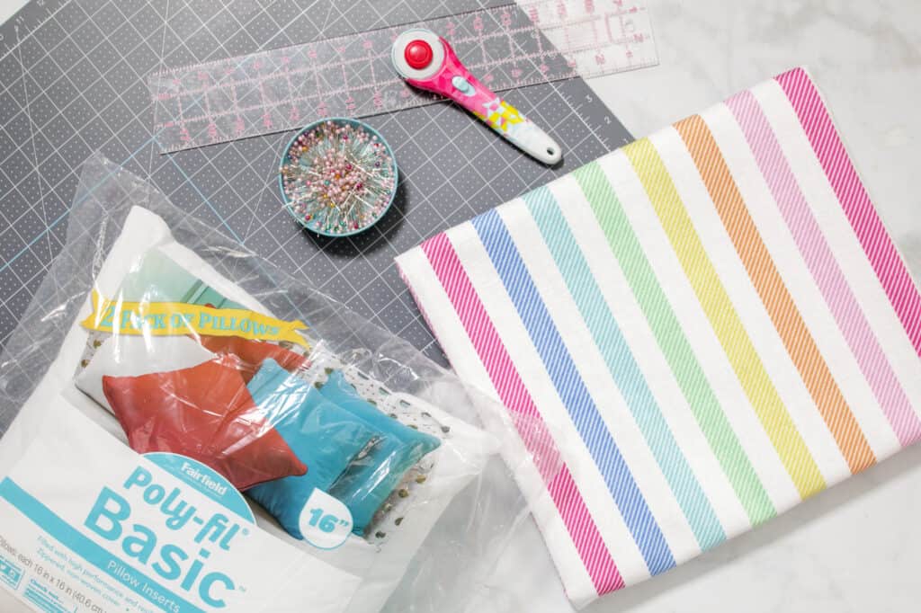 Supplies for Sewing an Envelope Pillow |How to Make an Envelope Pillow Cover With One Piece of Fabric by popular Utah sewing blog, Sweet Red Poppy: image of rainbow stripe fabric, rotary cutter, fabric pins and a rotary board. 