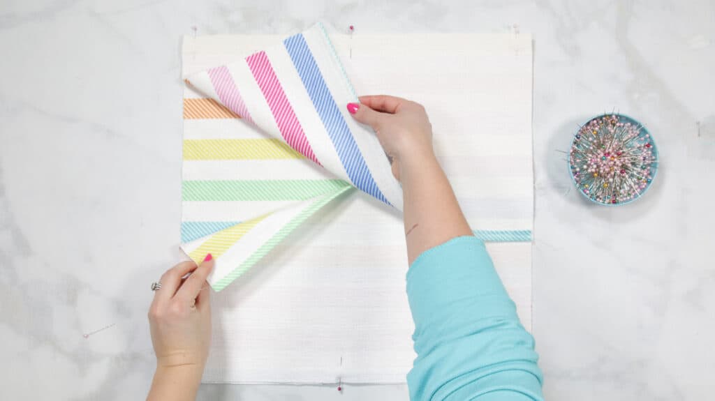 How to Make an Envelope Pillow Cover With One Piece of Fabric by popular Utah sewing blog, Sweet Red Poppy: image of a woman pinning together rainbow stripe fabric. 