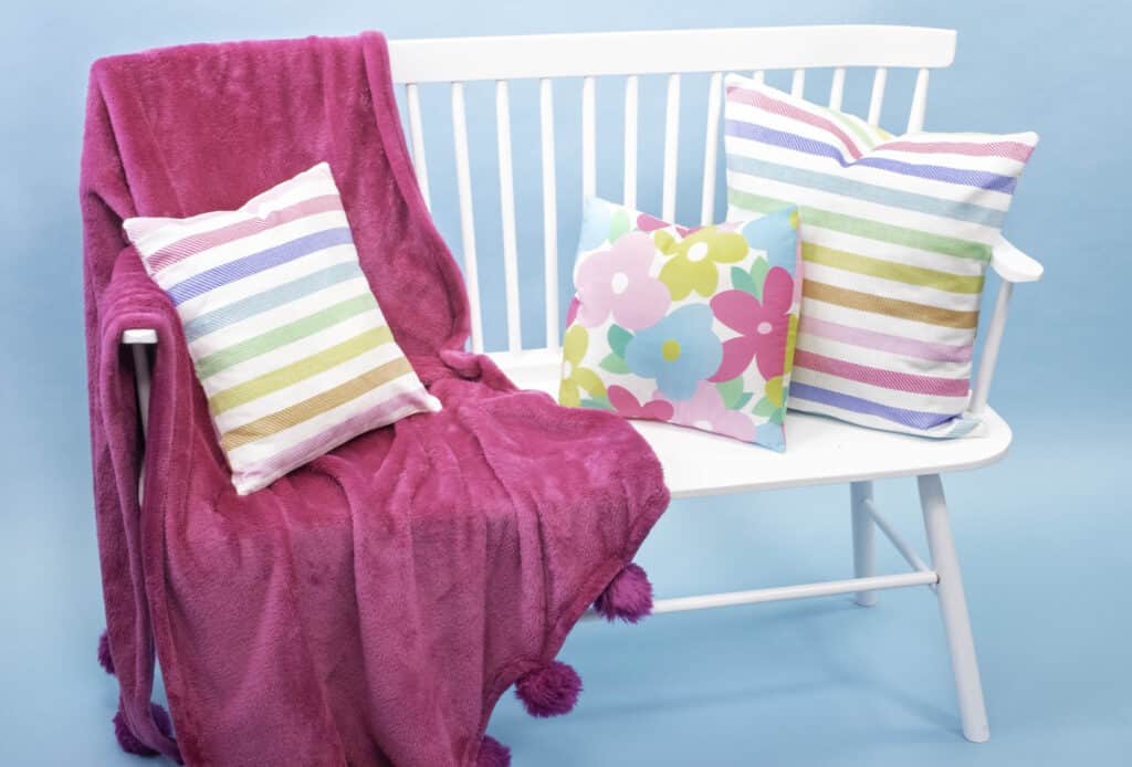 How to Make an Envelope Pillow Cover With One Piece of Fabric by popular Utah sewing blog, Sweet Red Poppy: image of floral print and rainbow stripe print envelope pillow covers on a white bench with a pink throw blanket. 