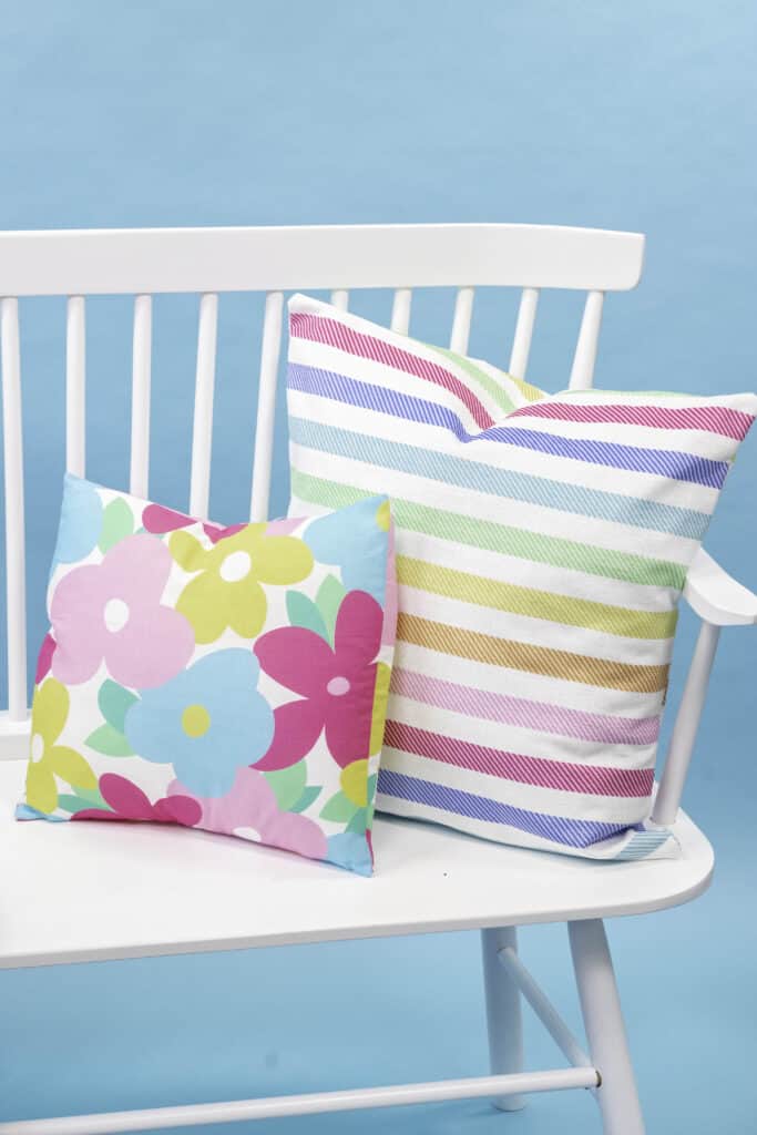 Learn How to Sew an Envelope Pillow Cover |How to Make an Envelope Pillow Cover With One Piece of Fabric by popular Utah sewing blog, Sweet Red Poppy: image of floral print and rainbow stripe print envelope pillow covers on a white bench.