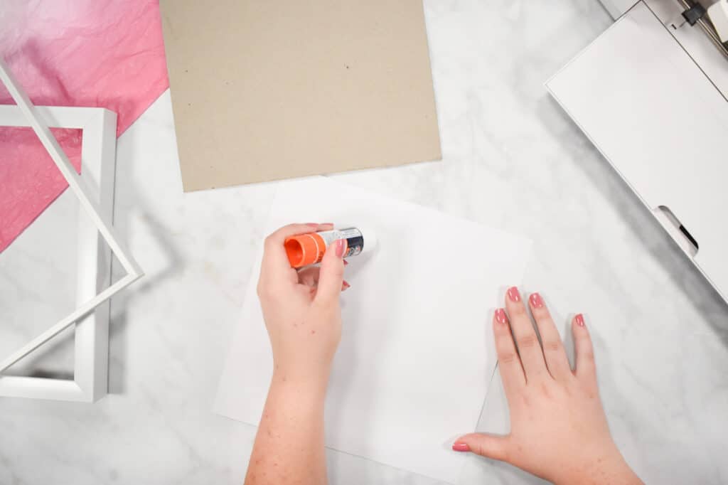 Cricut Shadow Box by popular US craft blog, Sweet Red Poppy: image of  a woman using a glue stick on a piece of white cardstock. 