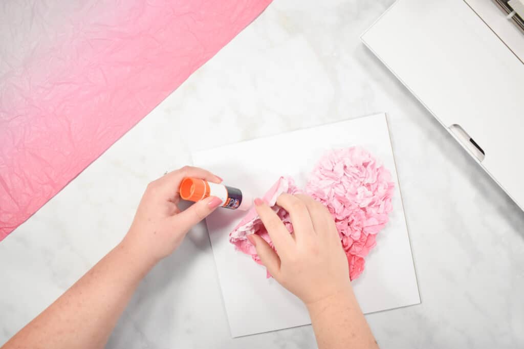 Cricut Shadow Box by popular US craft blog, Sweet Red Poppy: image of a woman gluing down a pink paper heart onto a piece of white cardstock. 