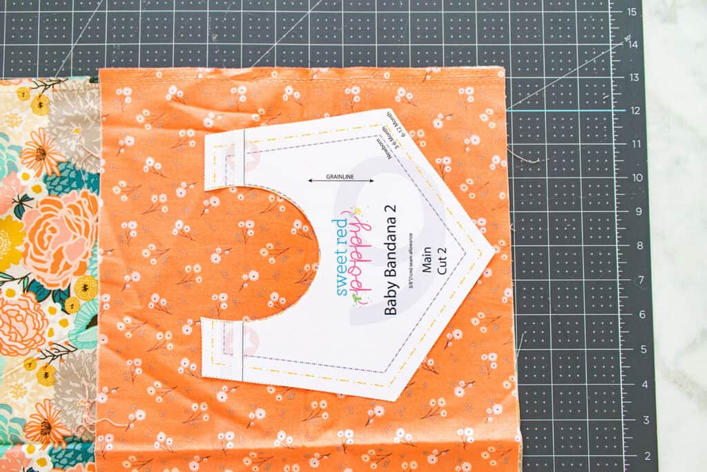 Baby Bib Sewing Pattern by popular US sewing blog, Sweet Red Poppy: image of fat quarters cotton fabric and a bib sewing pattern on a rotary mat. 