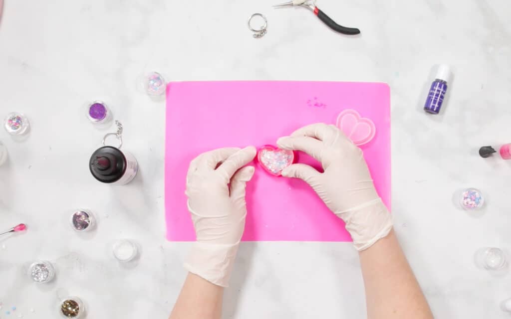 UV Resin by popular US craft blog, Sweet Red Poppy: image of a woman putting glitter n her resin mold on a pink resin mat. 