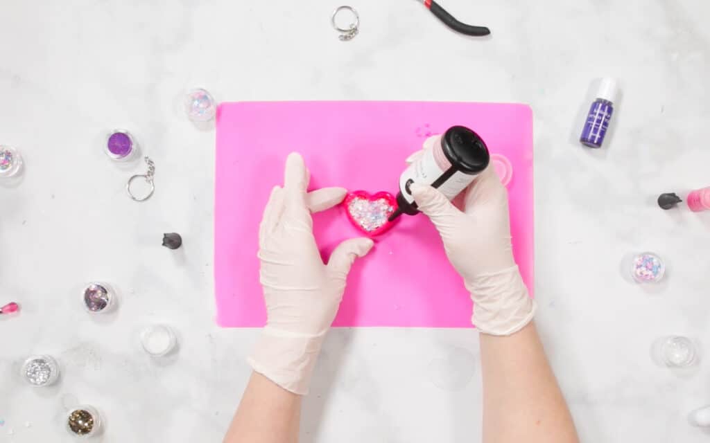 UV Resin by popular US craft blog, Sweet Red Poppy: image of a woman putting glitter n her resin mold on a pink resin mat. 