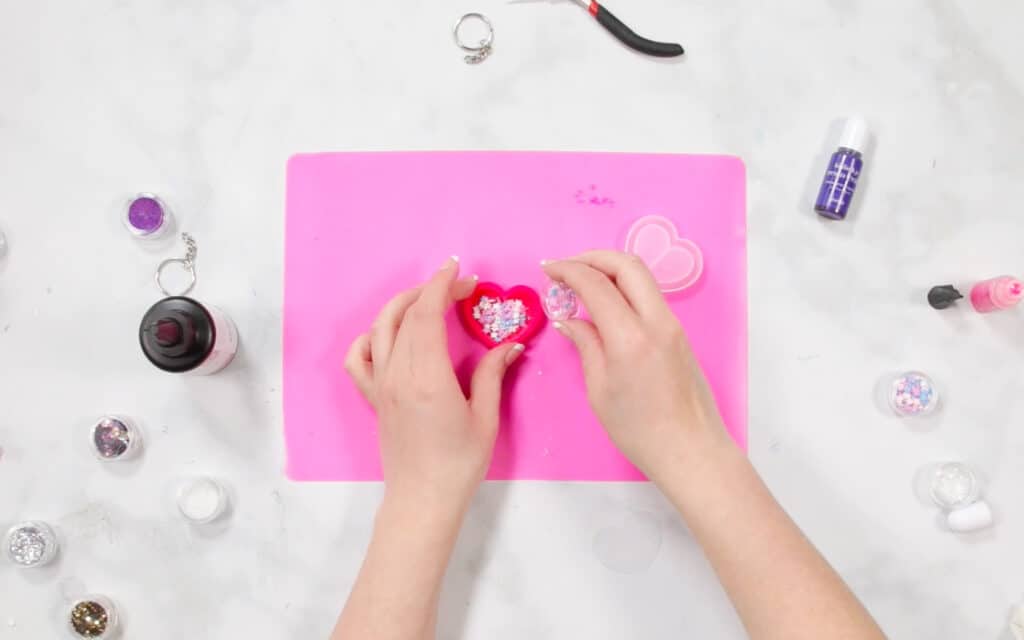 UV Resin by popular US craft blog, Sweet Red Poppy: image of a woman putting glitter n her resin mold on a pink resin mat. 