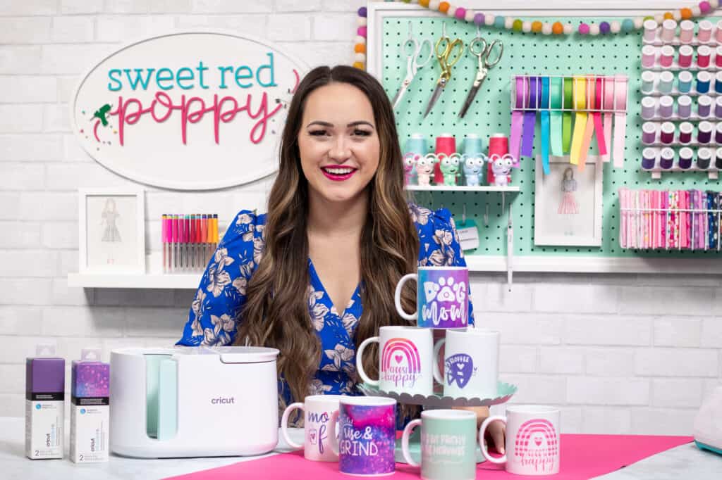 Cricut mug press review featured by top Cricut blogger, Sweet Red Poppy | Cricut Mug Press by popular US craft blog, Sweet Red Poppy: image of a woman standing behind a Cricut mug press and various white ceramic mugs. 