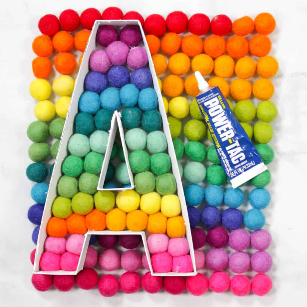 Felt Ball Letters by popular US craft blog, Sweet Red Poppy: image of a letter A filled with rainbow felt balls next to a tube of Power Tac. 