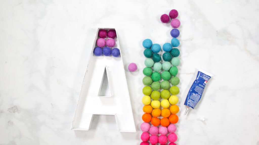 Felt Ball Letters by popular US craft blog, Sweet Red Poppy: image of a white cardboard letter A next to a row  of rainbow felt balls. 