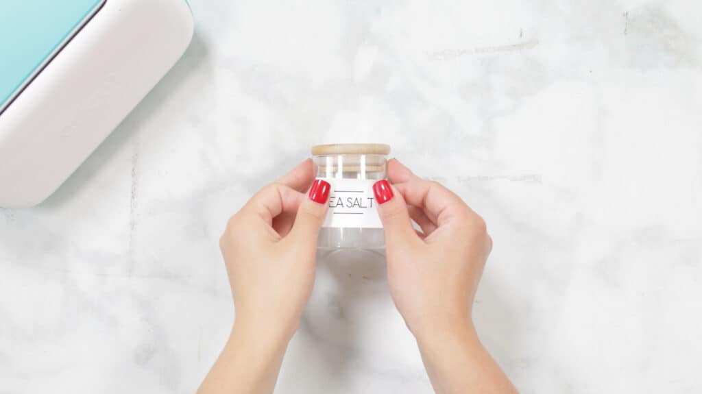 Apply Label |Kitchen Organization Hacks by popular US craft blog, Sweet Red Poppy: image of a woman applying a Cricut Joy Smart Label to a glass spice jar. 