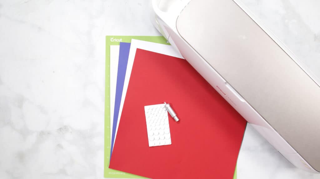 DIY 4th of July Wreath by popular US craft blog, Sweet Red Poppy: image of red, white,and blue paper next to a Cricut machine. 