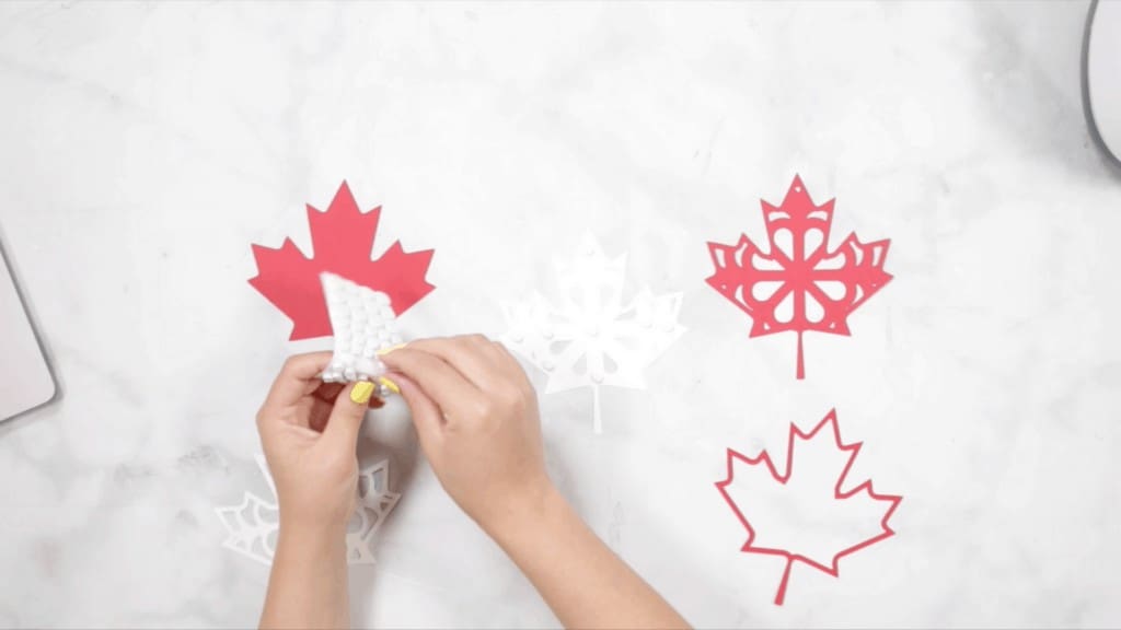 Canada Day Wreath by popular US craft blog, Sweet Red Poppy: image of some red and white paper maple leaves and a woman peeling off a sticky dot. 