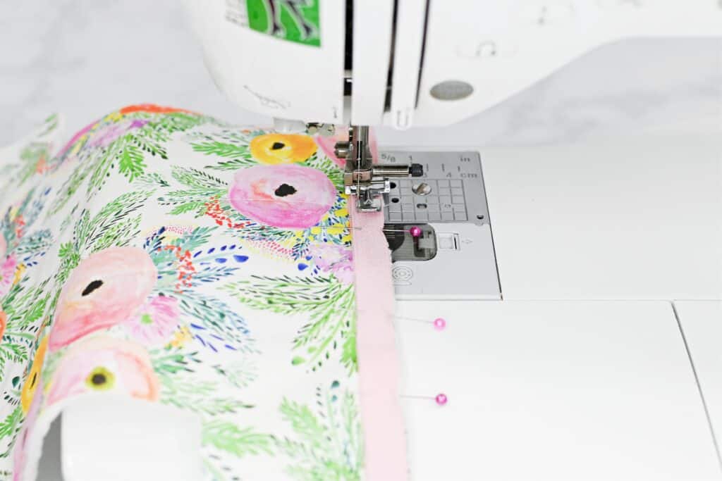 Zippered Box Pouch by popular US sewing blog, Sweet Red Poppy: image of a pink zipper being sewn to some floral fabric on a white sewing machine. 