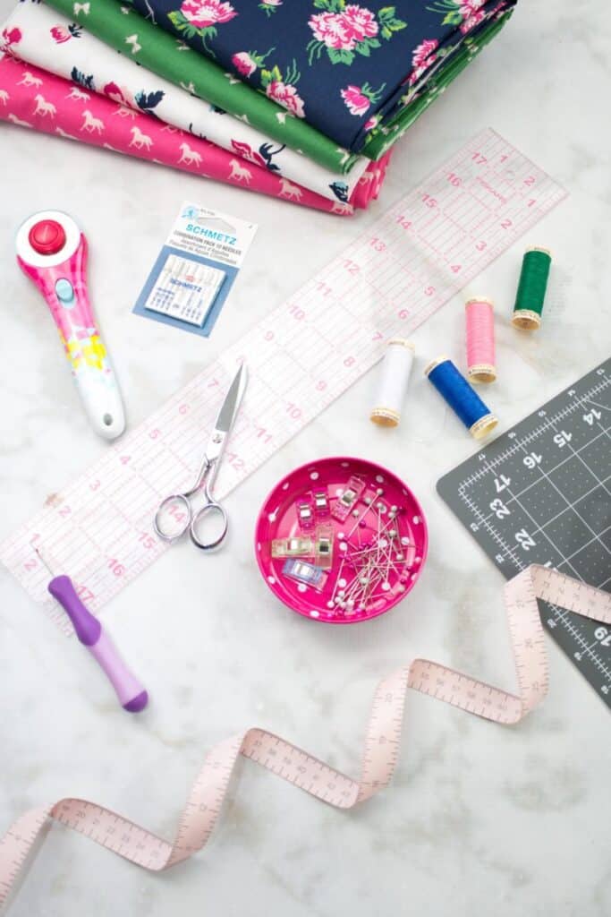 Sewing Supplies. |Serger VS Sewing Machine by popular US sewing blog, Sweet Red Poppy: image of fabric, rotary board, scissors, rotary cutter, needles, and a measuring tape. 