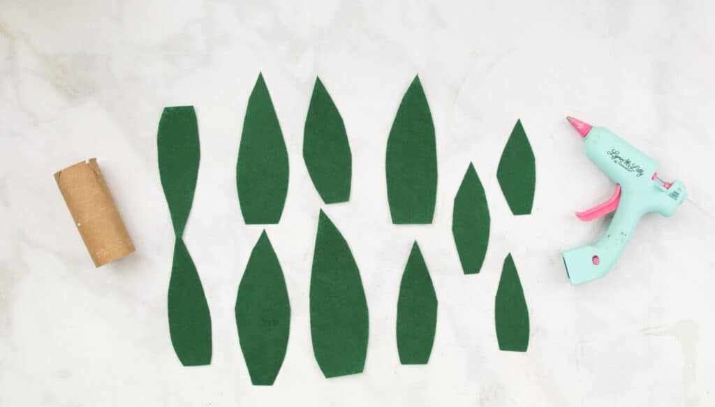 Showing a Paper Roll, Hot Glue Gun, and Three Large, Medium and Small Green Leaves Cut Out of Felt.