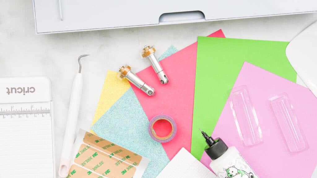 Showing supplies needed for gift card holders: Cutting machine, double & single scoring wheel, weeder, craft glue, and plastic tube with adhesive