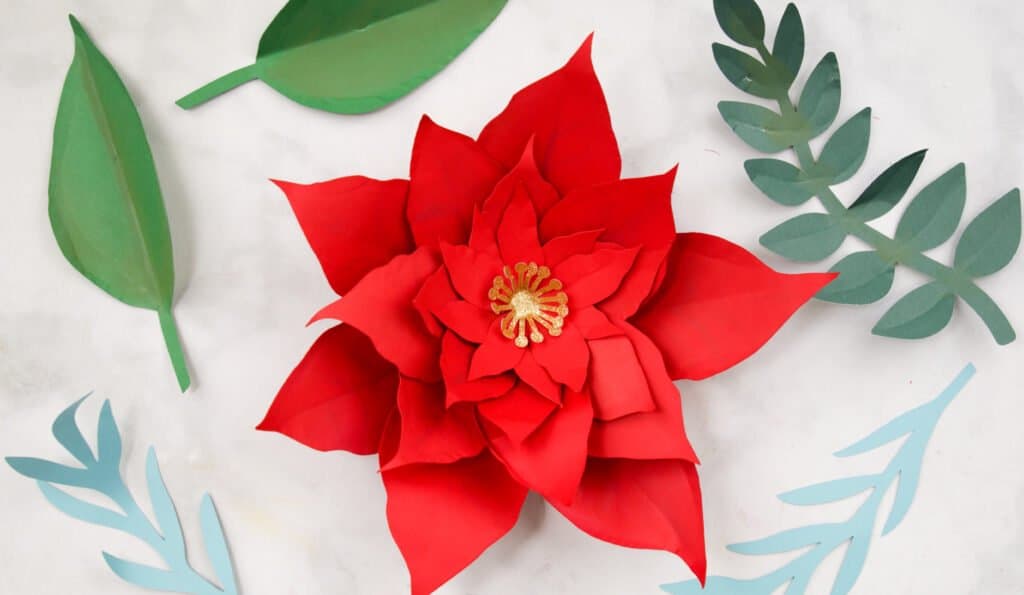 Finished Poinsettia Paper Flower surrounded by leaves. 