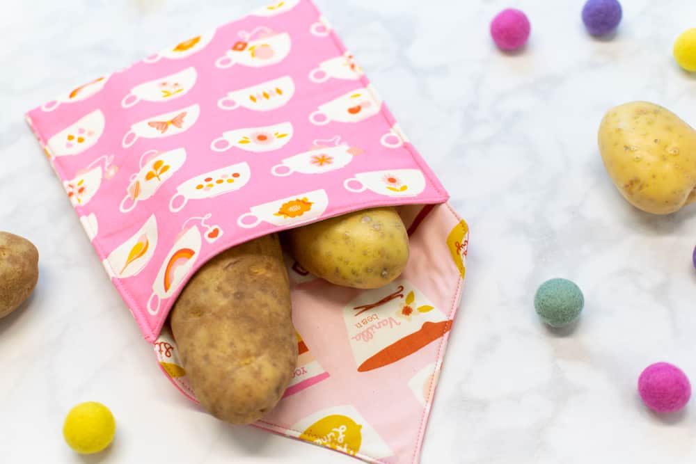 a closeup angled view of a pink microwave potato bag with two potatoes inside and two more potatoes next to it