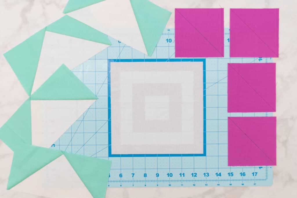 a large white square centered on a cutting mat surrounded by flying geese and 4 small pink squares