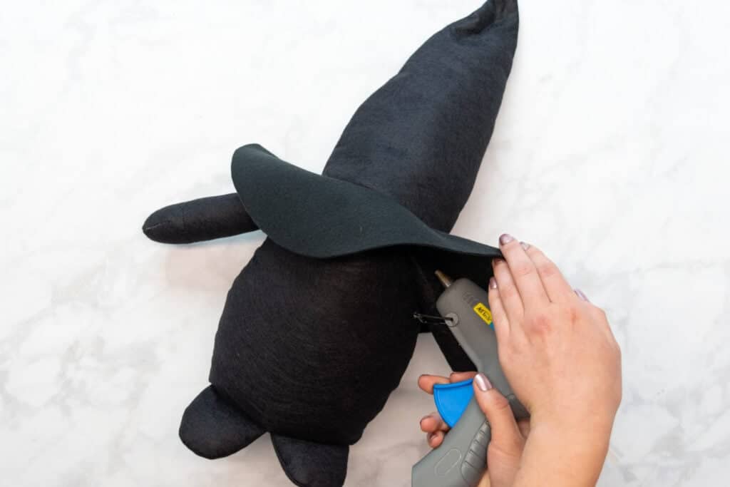gluing the brim of the hat to the arms of the gnome with a grey hot glue gun