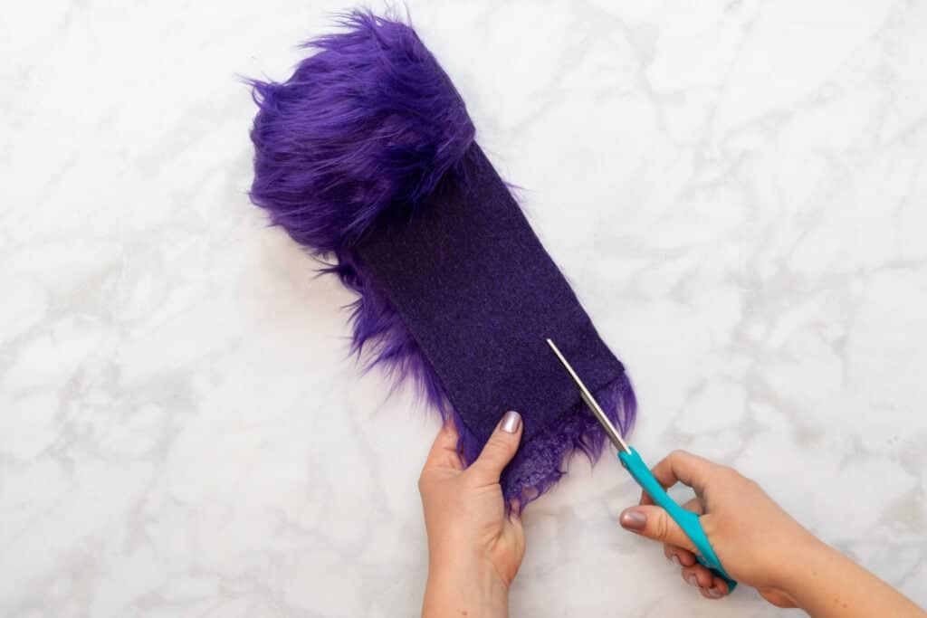 cutting a strip of purple faux fur with a pair of turquoise scissors