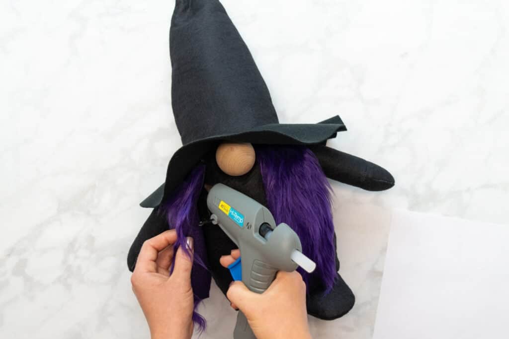 gluing the purple hair to either side of the wooden nose with a grey hot glue gun