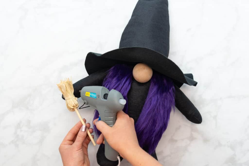 gluing the witch broom to the gnome's hand with a grey hot glue gun