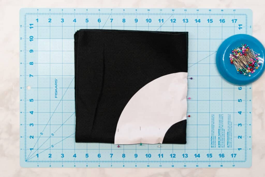 hat brim pattern pinned to black felt on a blue cutting mat