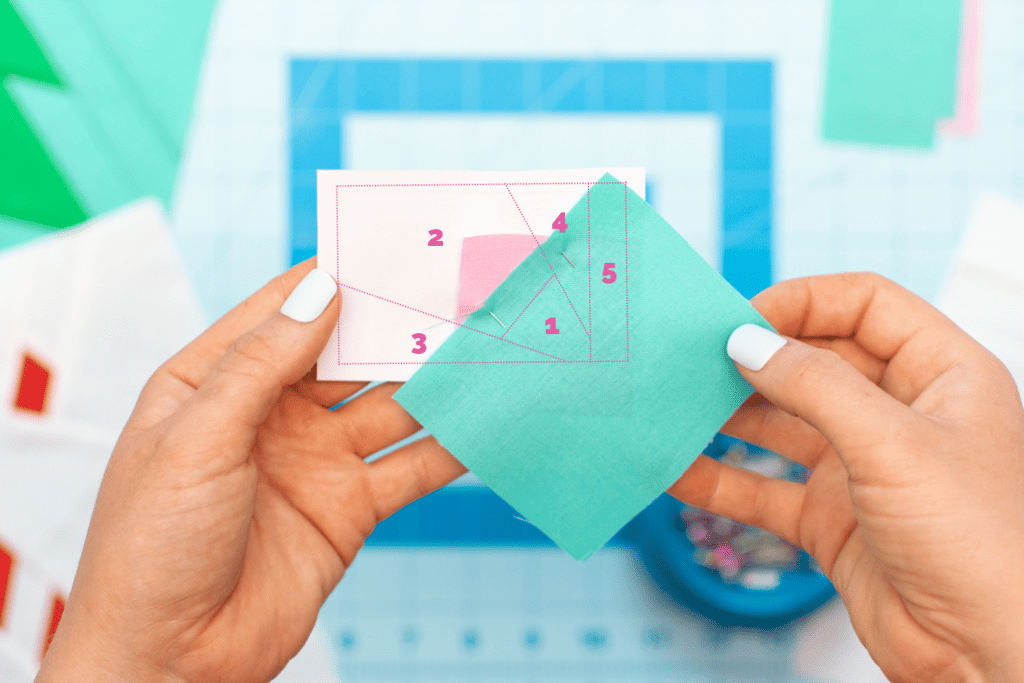a piece of green fabric is pinned to a square of pink fabric on a paper template
