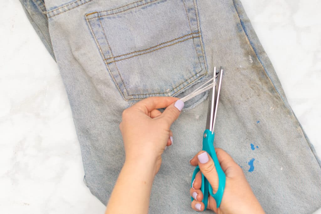 trimming a rip in jeans with turquoise scissors
