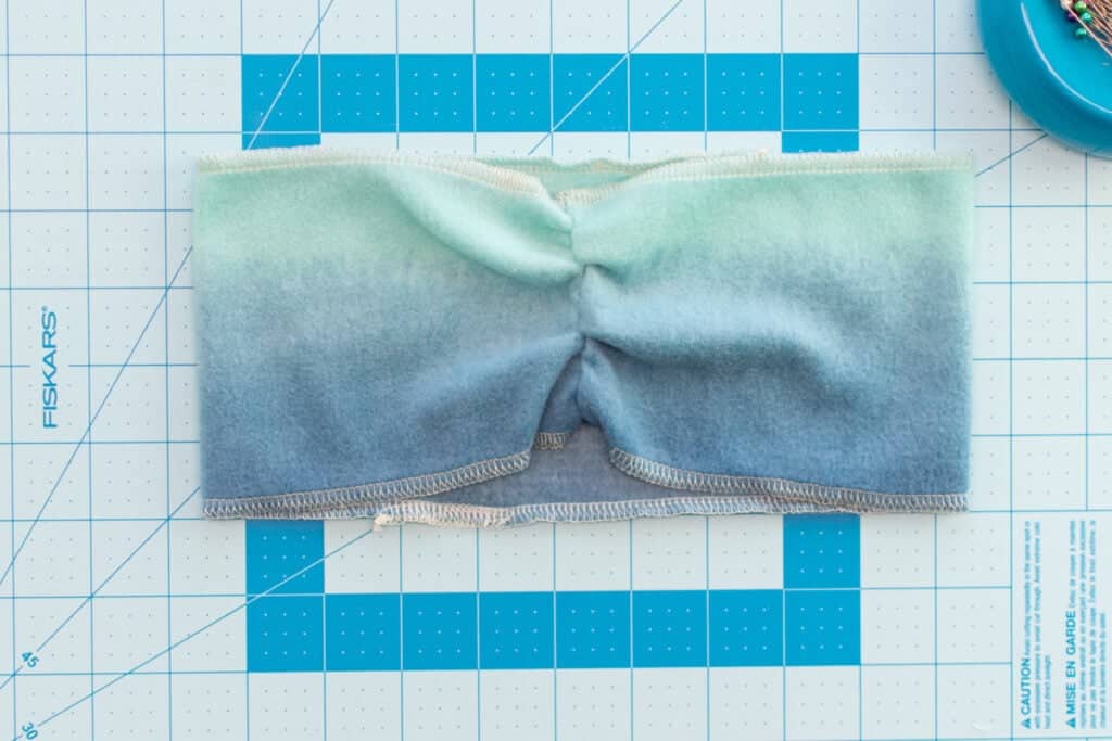 the top and bottom edges of the blue ombre fleece headband with gathered front seam have been finished with a serger stitch using white thread