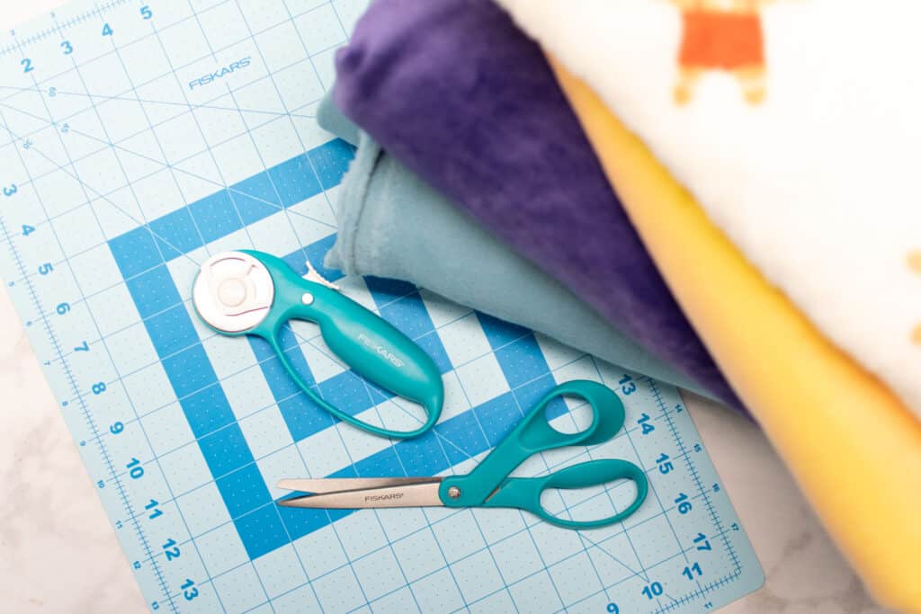 a stack of fleece fabric next to a blue cutting mat and turquoise cutting tools