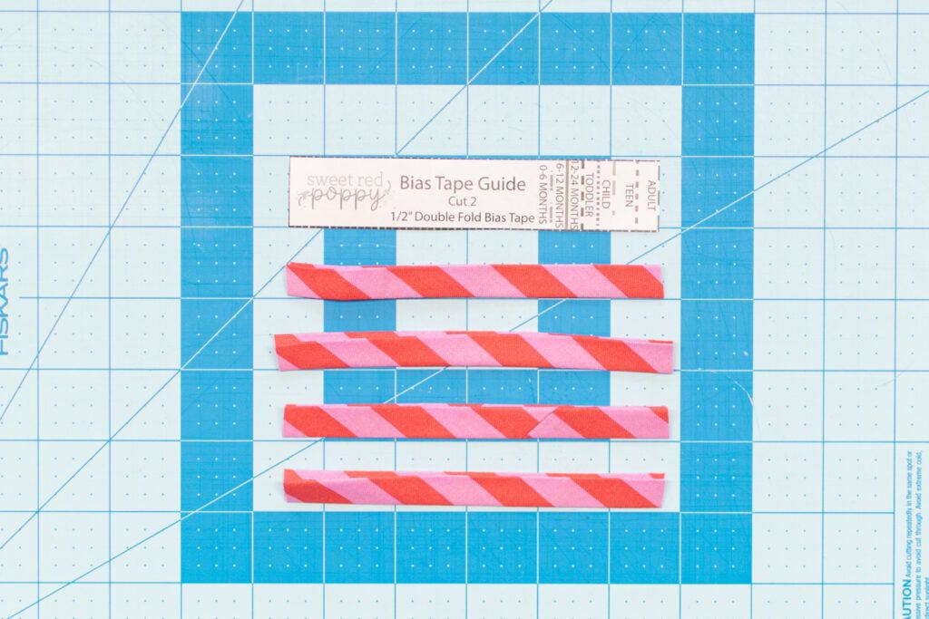 four pieces of pink striped bias tape cut and placed on a blue cutting mat