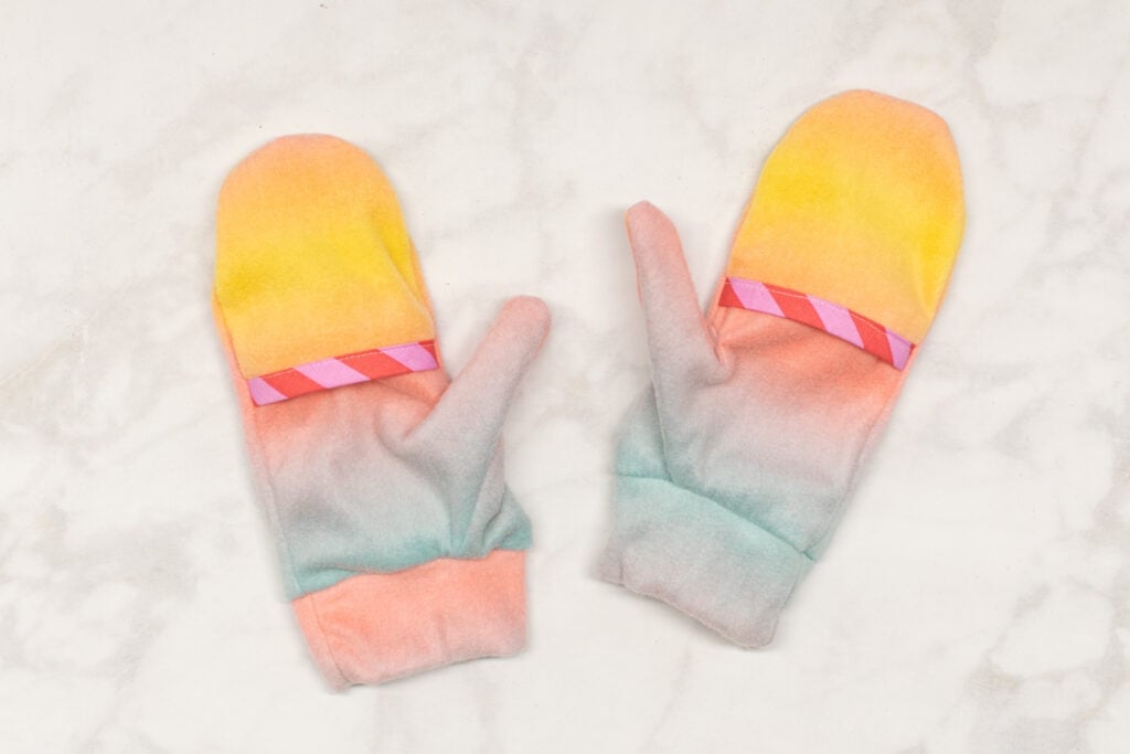 the finished ombre fleece mittens are laying on a marble backdrop