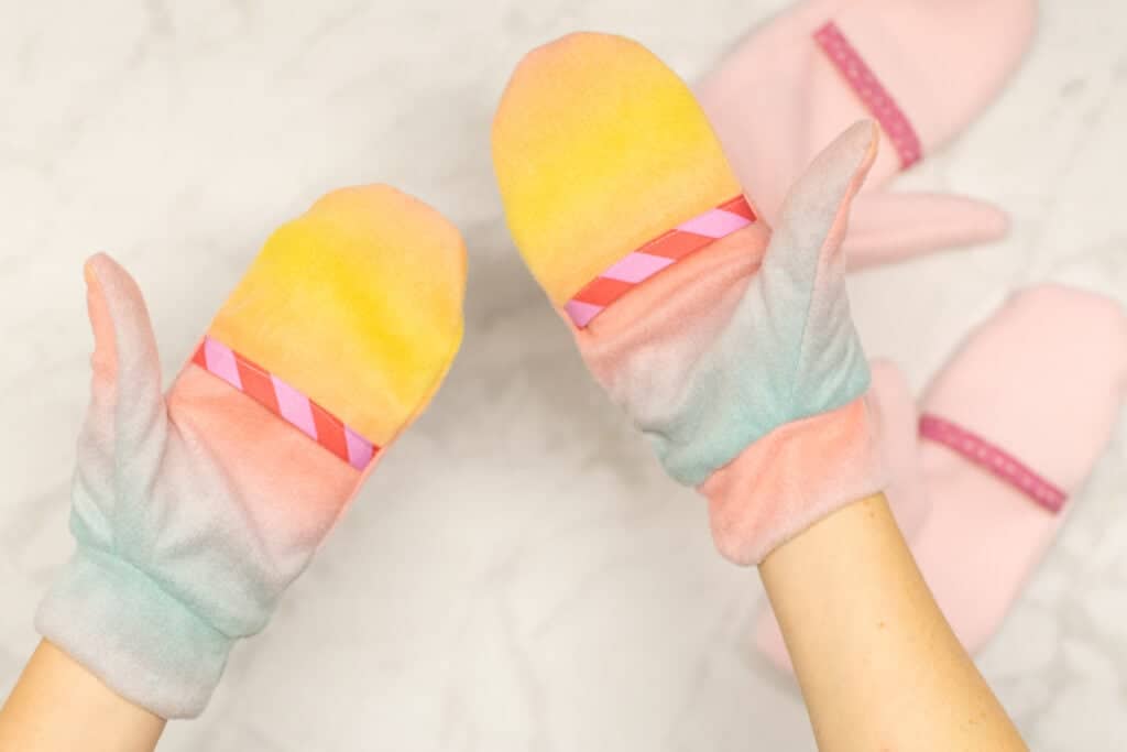 wearing a pair of ombre fleece mittens with light pink mittens in the background