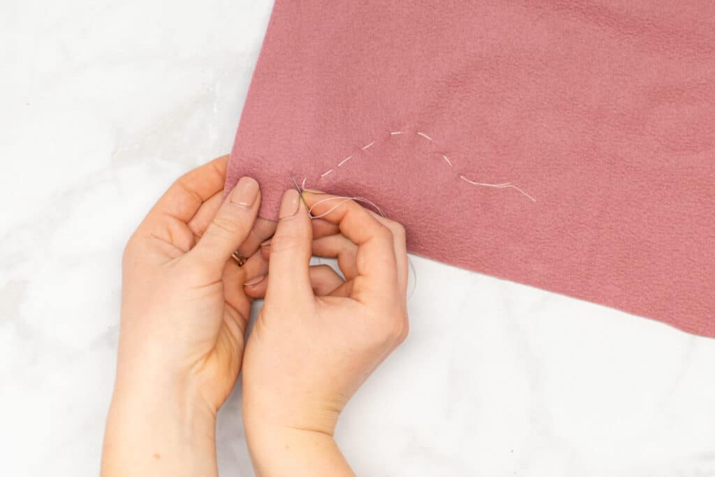 hand stitching long basting stitches with white thread on dark pink fabric