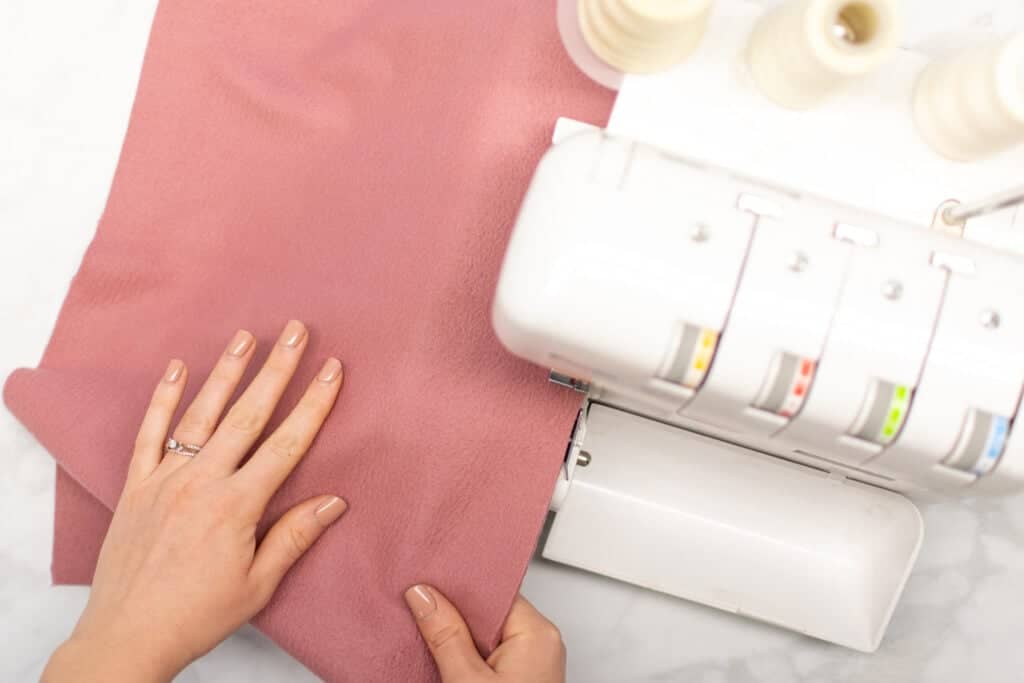 guiding a piece of pink fabric through a serger on a white backdrop