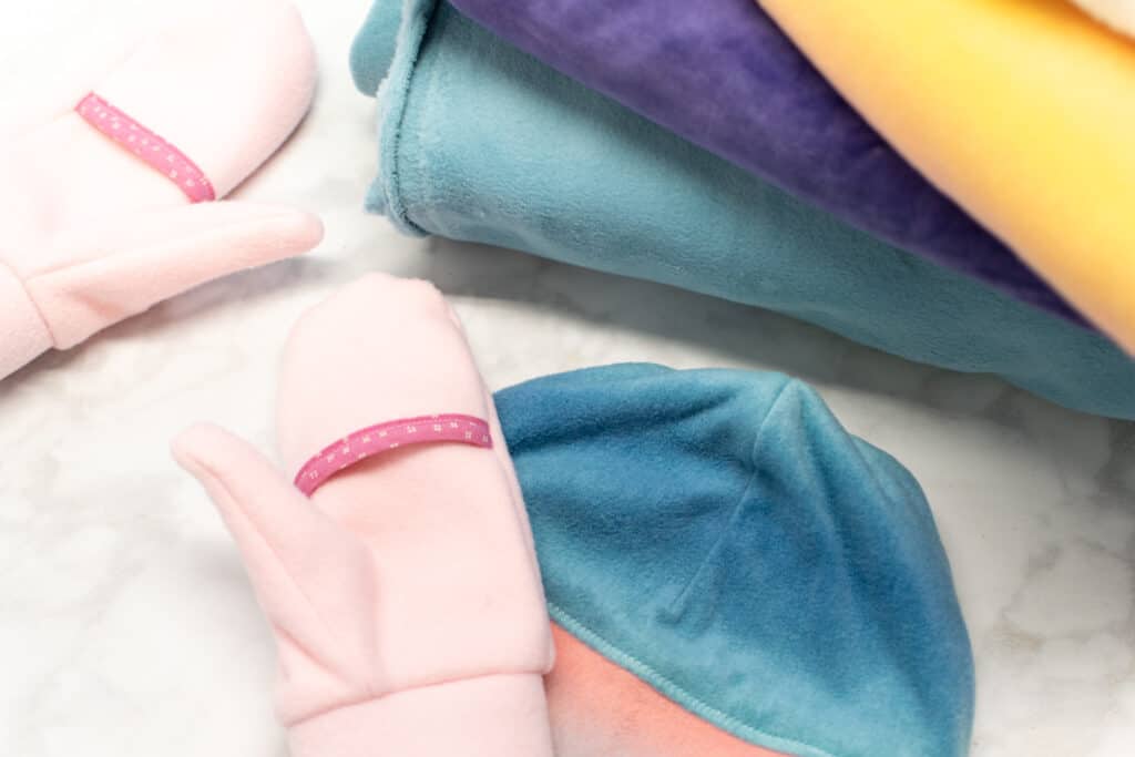 a stack of fleece fabric next to pink mittens and a blue hat