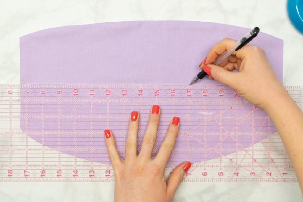 a clear quilting ruler laid across the heating pad while marking a straight line with a fabric pen