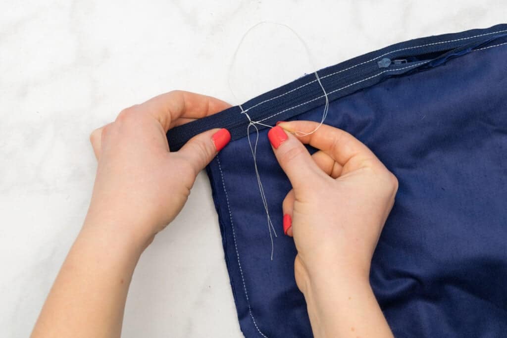 sewing a new zipper stop with a hand sewing needle and white thread