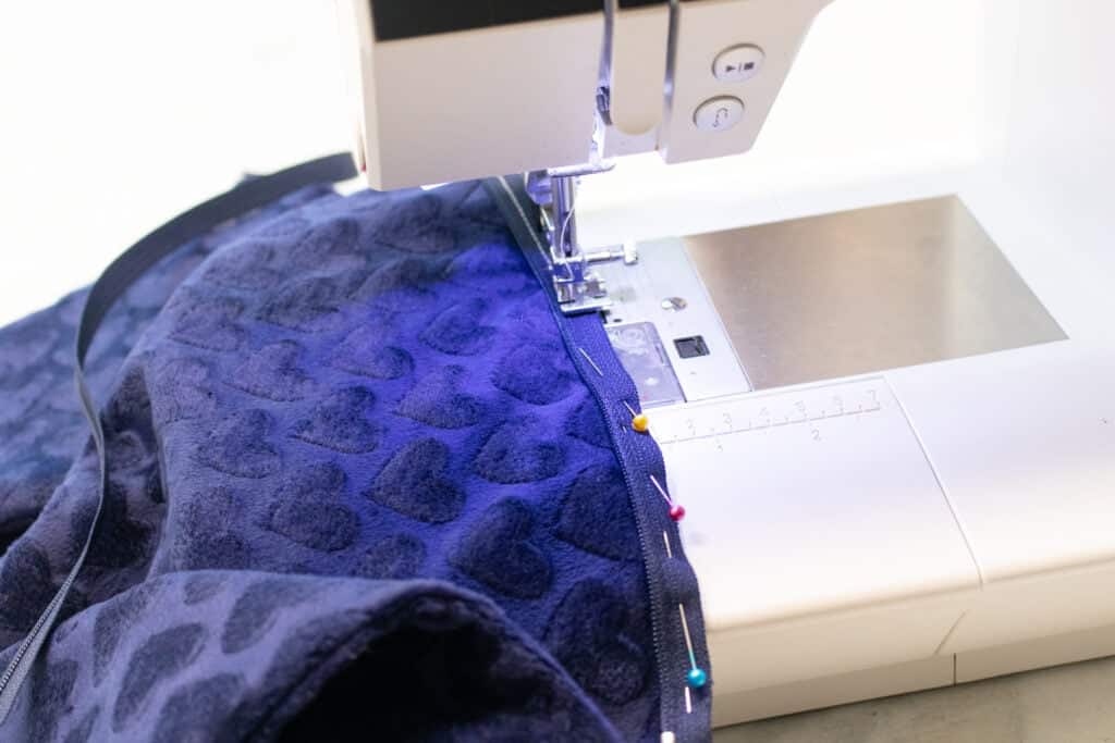 a closeup of a sewing machine stitching the zipper to the minky heart fabric with a zipper foot